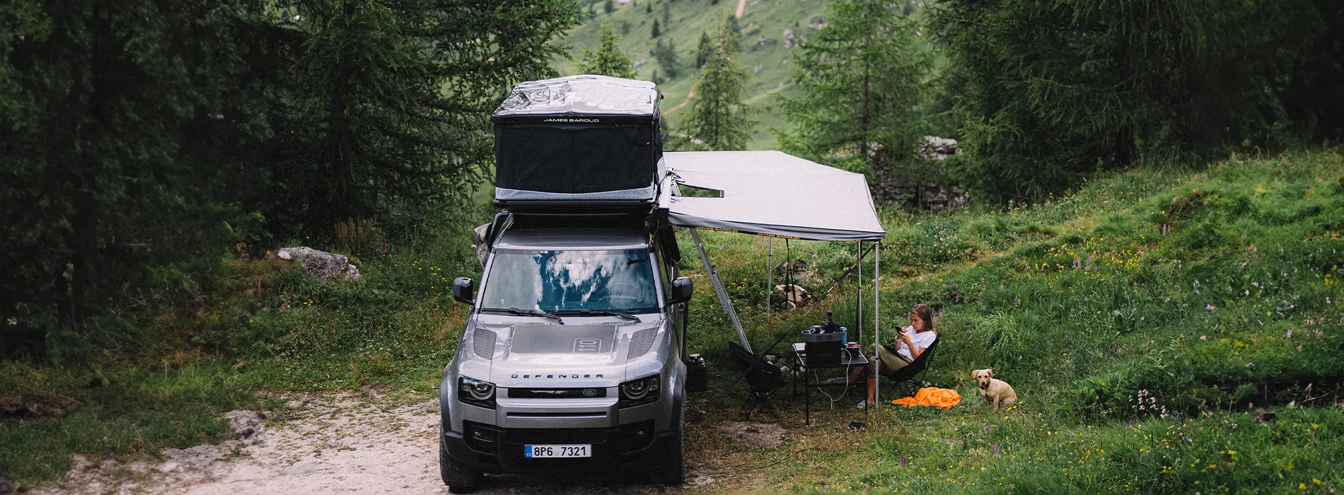 Katerina Hrnová Sitting with Dog in a Green Landscape under a Falcon Awning 270 and an Open Rooftop Tent, Setup on Car